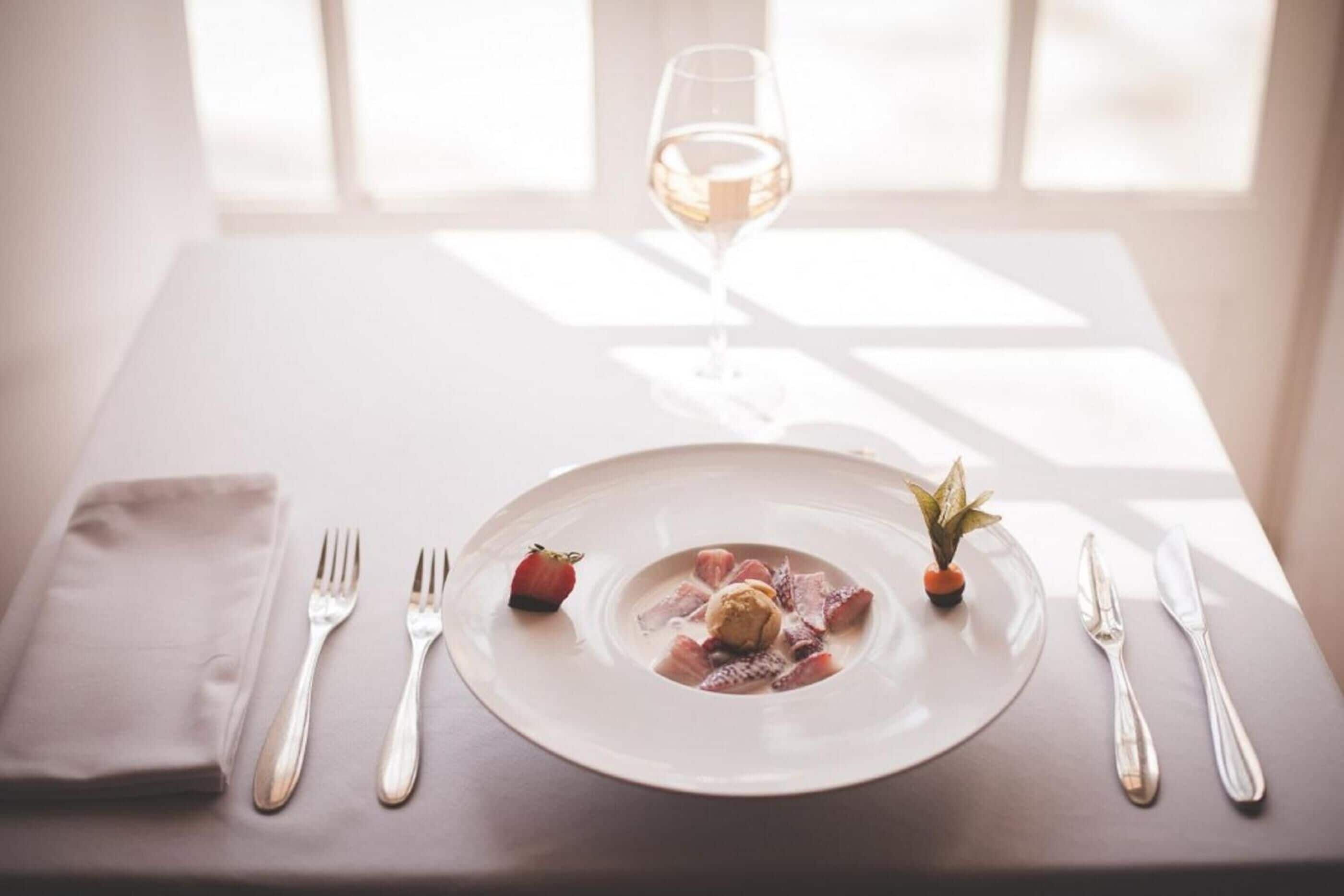A table set with a plate of food, a glass of white wine, and silverware.