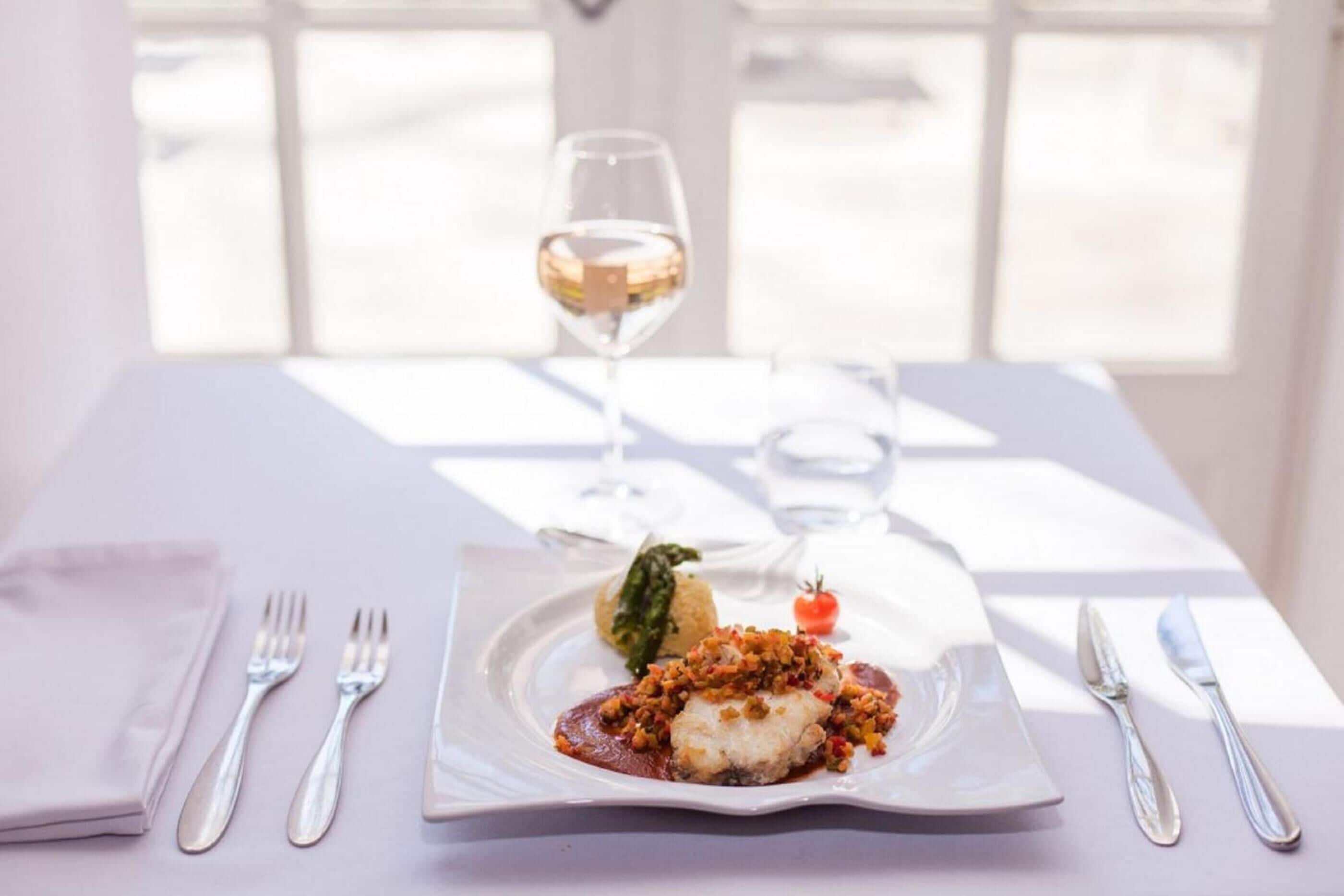 A dining table with a plate of food, a glass of wine, and cutlery.