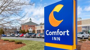 A Comfort Inn sign with a crescent moon logo, surrounded by a parking lot and a building with a green roof.