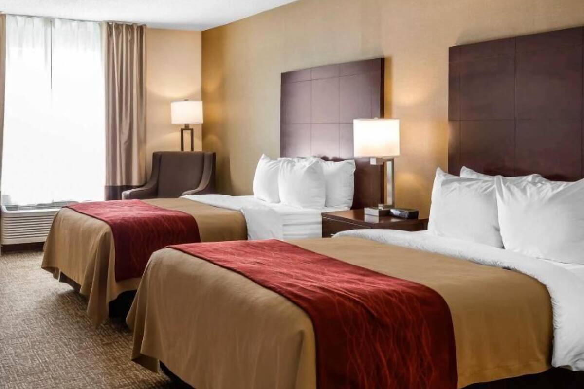 Une chambre d’hôtel avec deux lits, une chaise, un bureau et une lampe.
