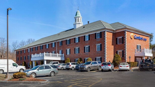 A Comfort Inn hotel with a brick facade, a central tower, and a parking lot with several cars.