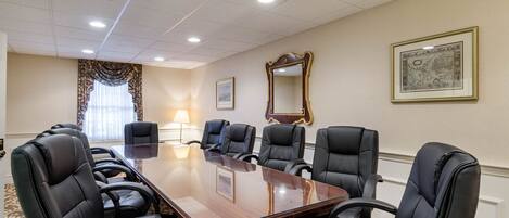 A conference room with a large rectangular table surrounded by black leather chairs, a large mirror on the wall, and a framed picture.
