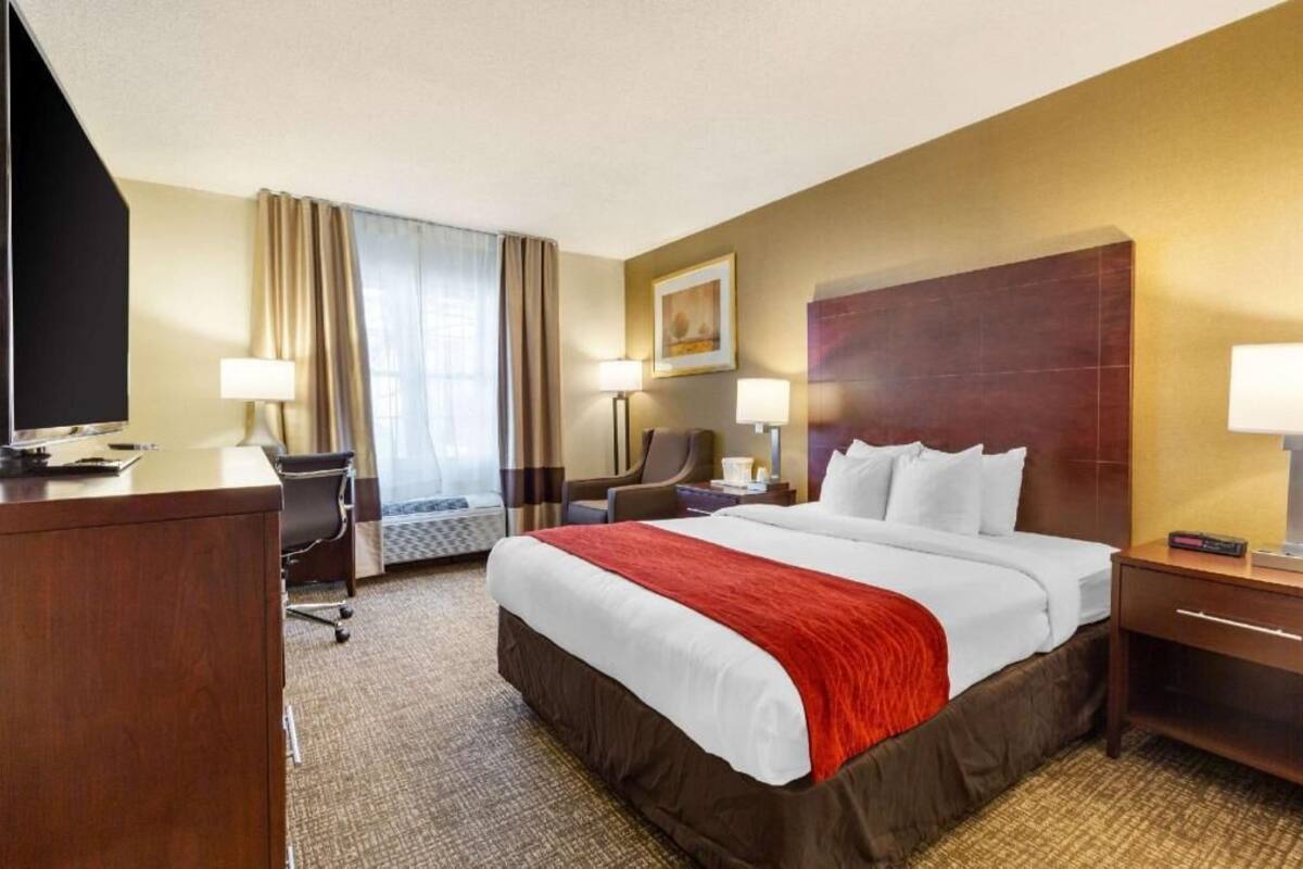 Une chambre d’hôtel avec un lit, un bureau, une chaise et une grande fenêtre avec des rideaux.