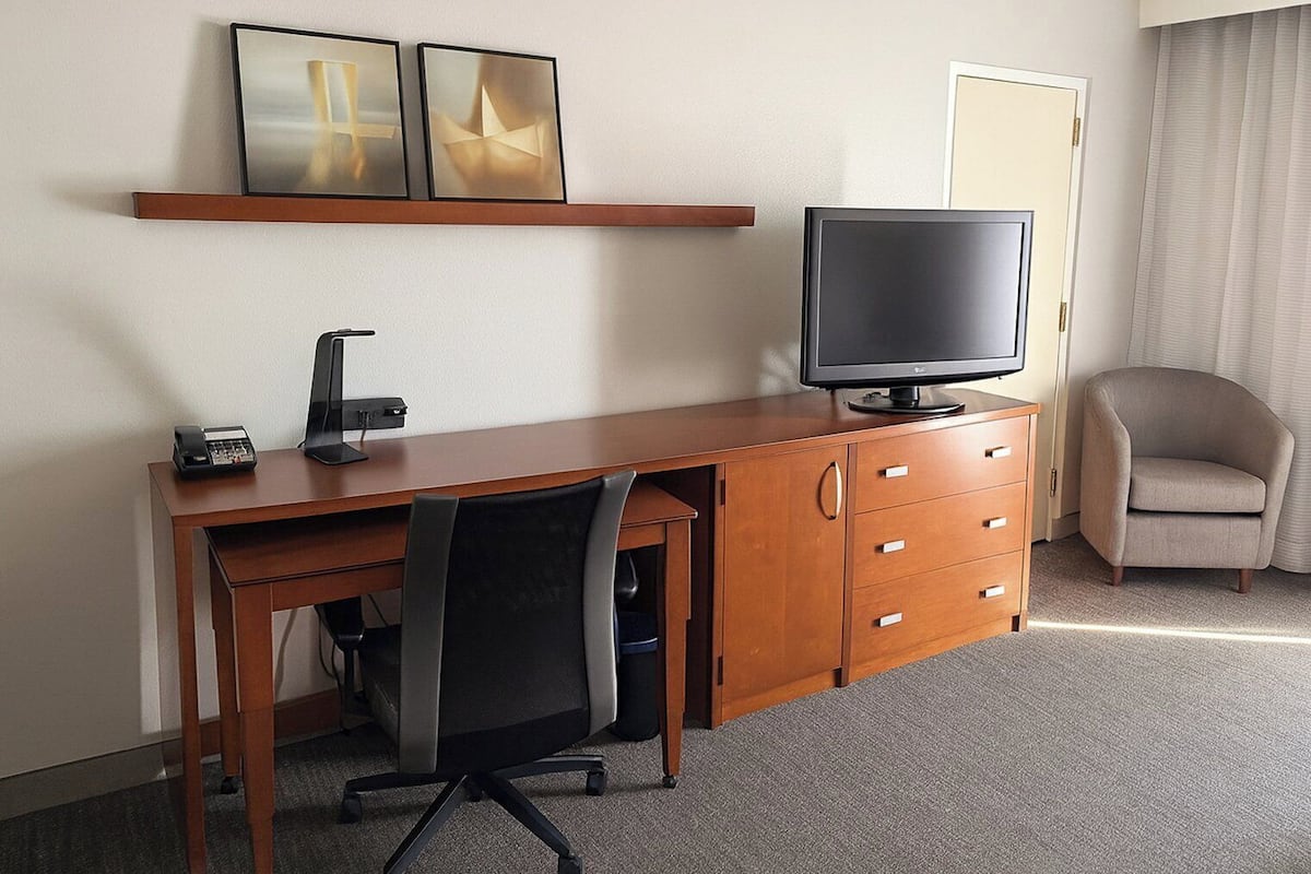 A hotel room with a wooden desk, a chair, a television, a telephone, and a door.