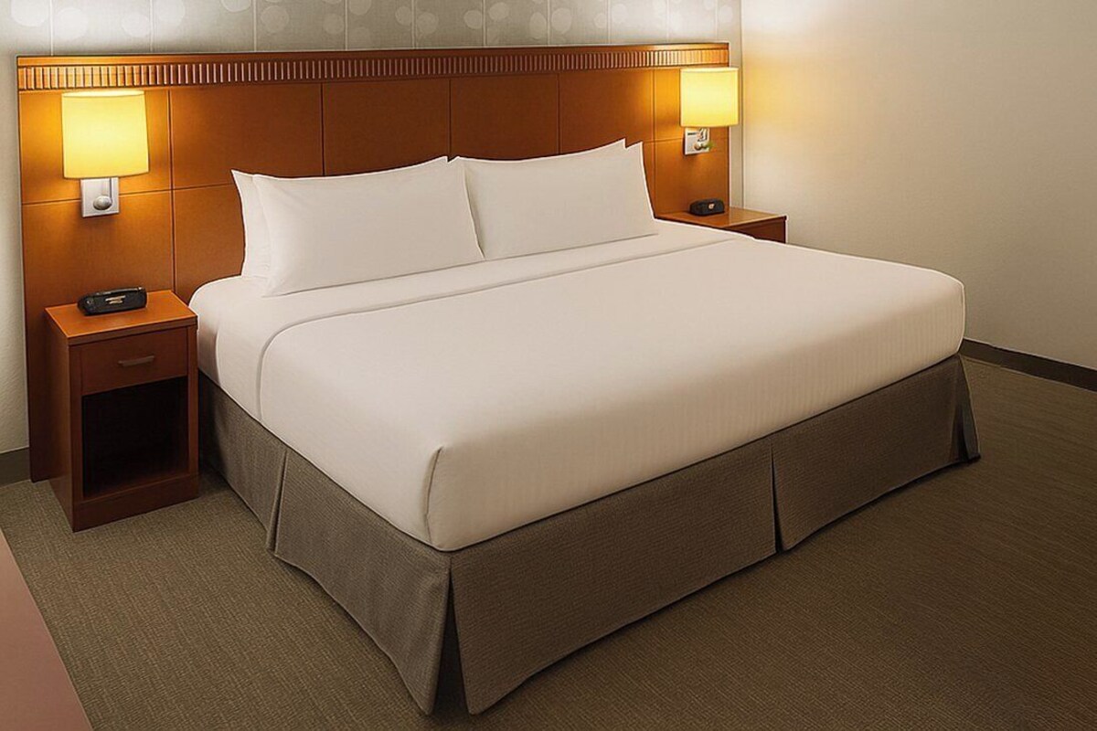 Una habitación de hotel con una cama grande, dos mesitas de noche con lámparas, un atril y suelo cubierto de alfombra.