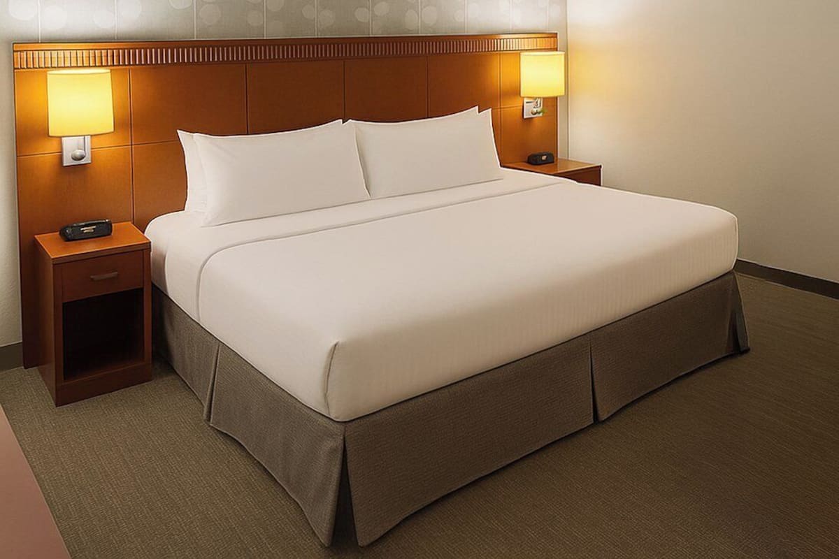 A hotel room with a large bed, two bedside tables with lamps, a nightstand, and a carpeted floor.