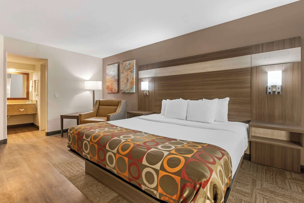 A hotel room with a large bed, a chair, a desk, and a mirror.