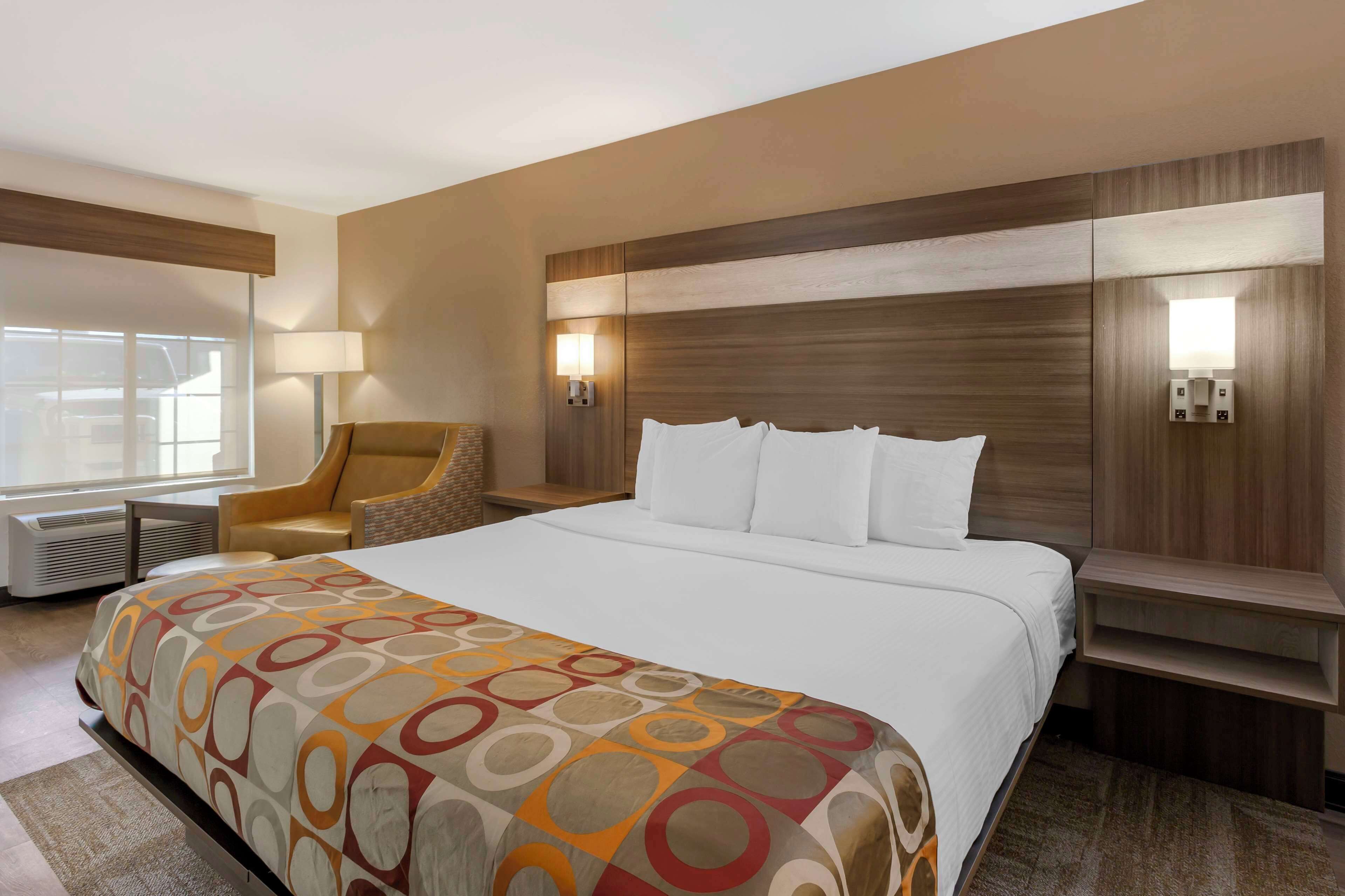 A hotel room with a large bed, a chair, a desk, and a lamp.