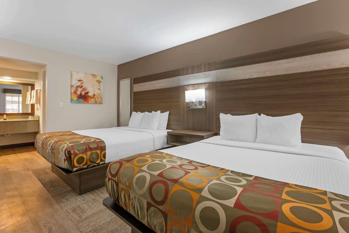 A hotel room with two beds, a large mirror, a painting on the wall, and a wooden headboard.