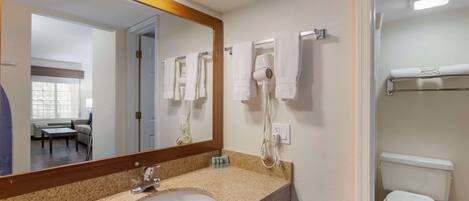 Un baño con lavamanos de granito, espejo, secador de pelo y un inodoro.