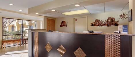 A reception area with a modern design, featuring a reception desk, a bench, and a large window providing a view of the outside.