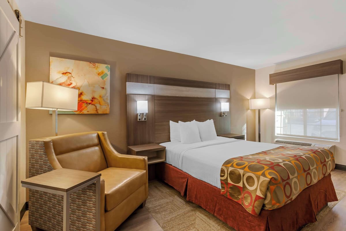 A hotel room with a bed, a desk, a chair, a headboard, and a wall-mounted artwork.