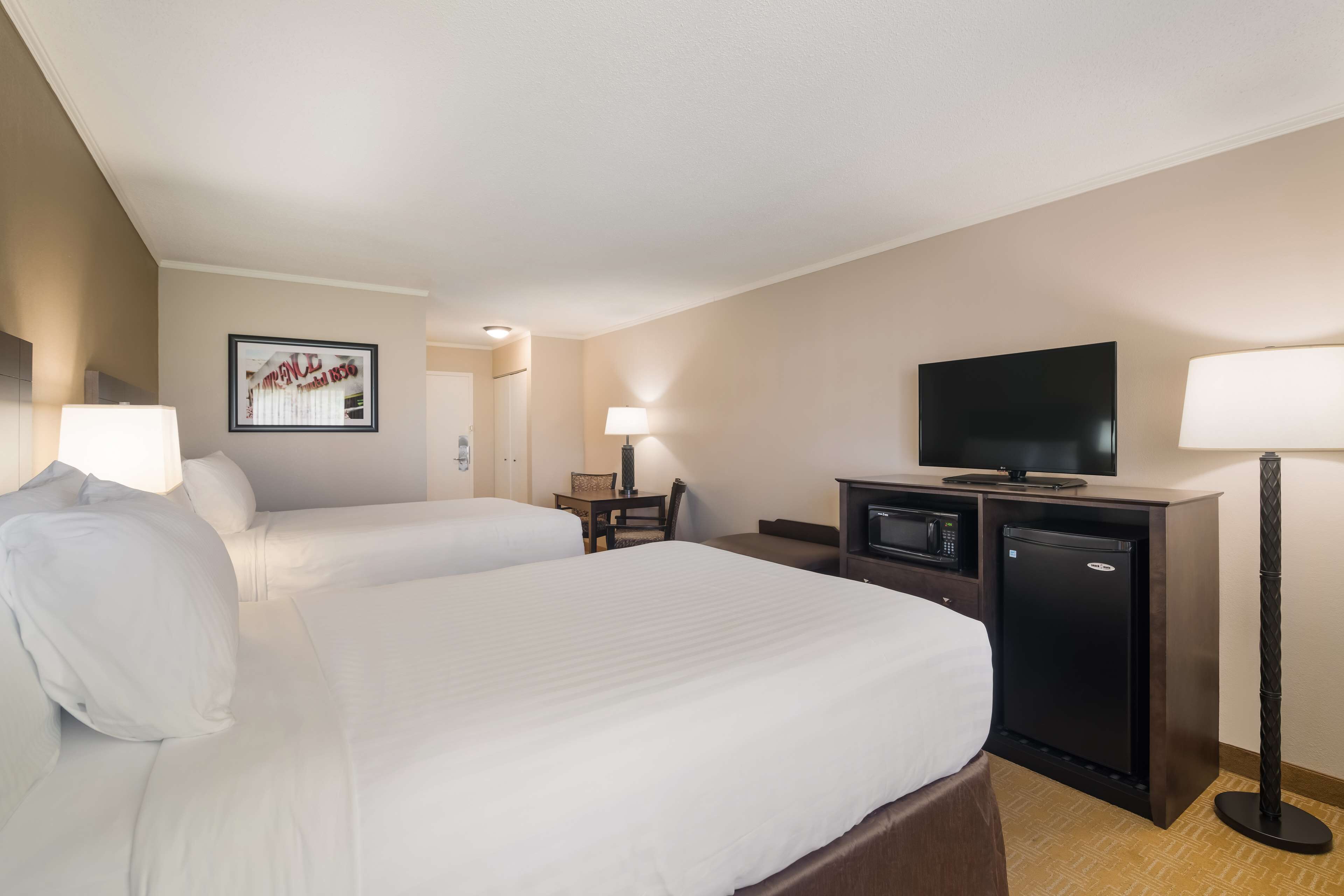 A hotel room with two beds, a television, a desk with a lamp, and a refrigerator.