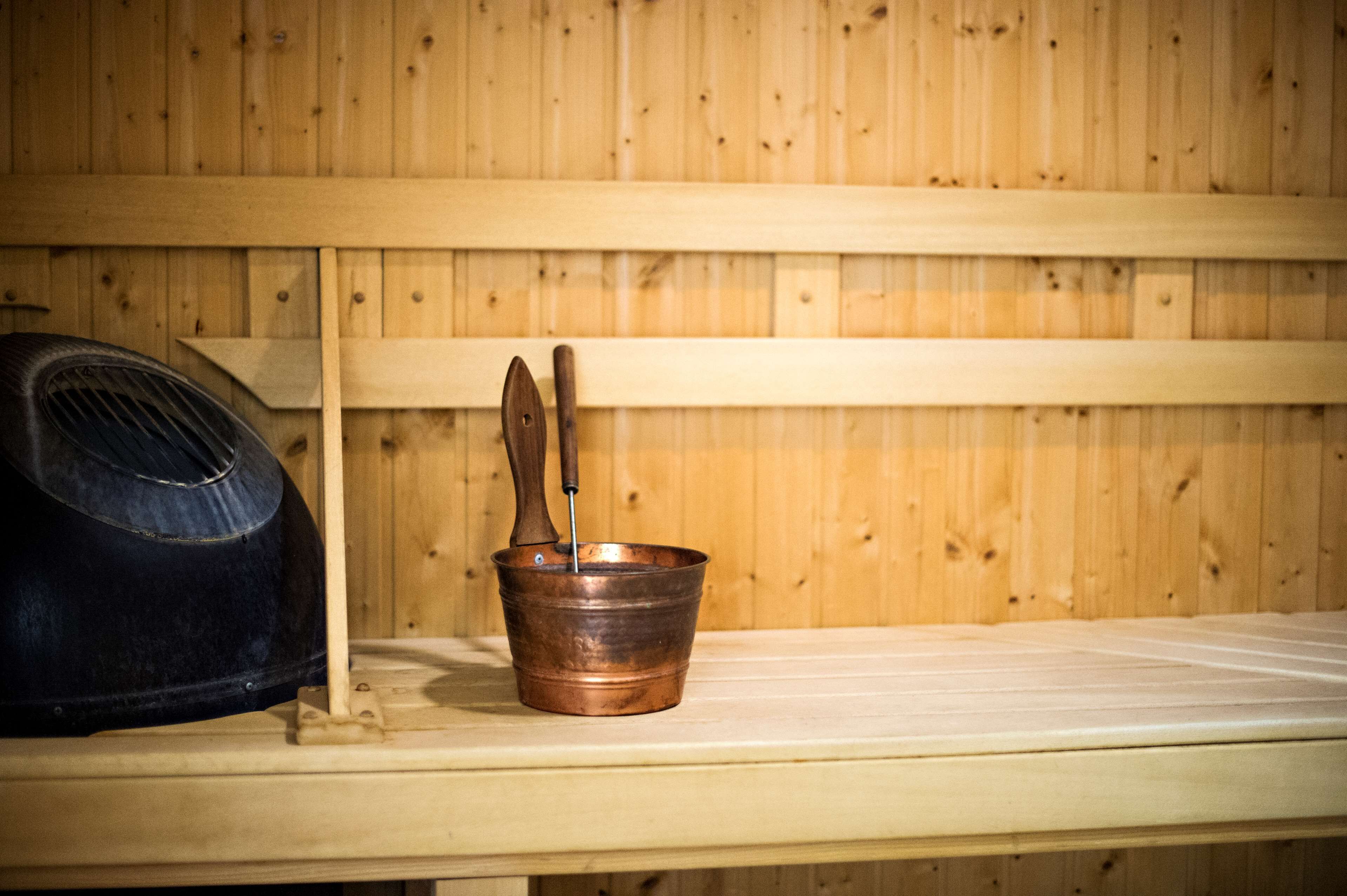 A wooden sauna bench with a copper bucket and a black sauna head.