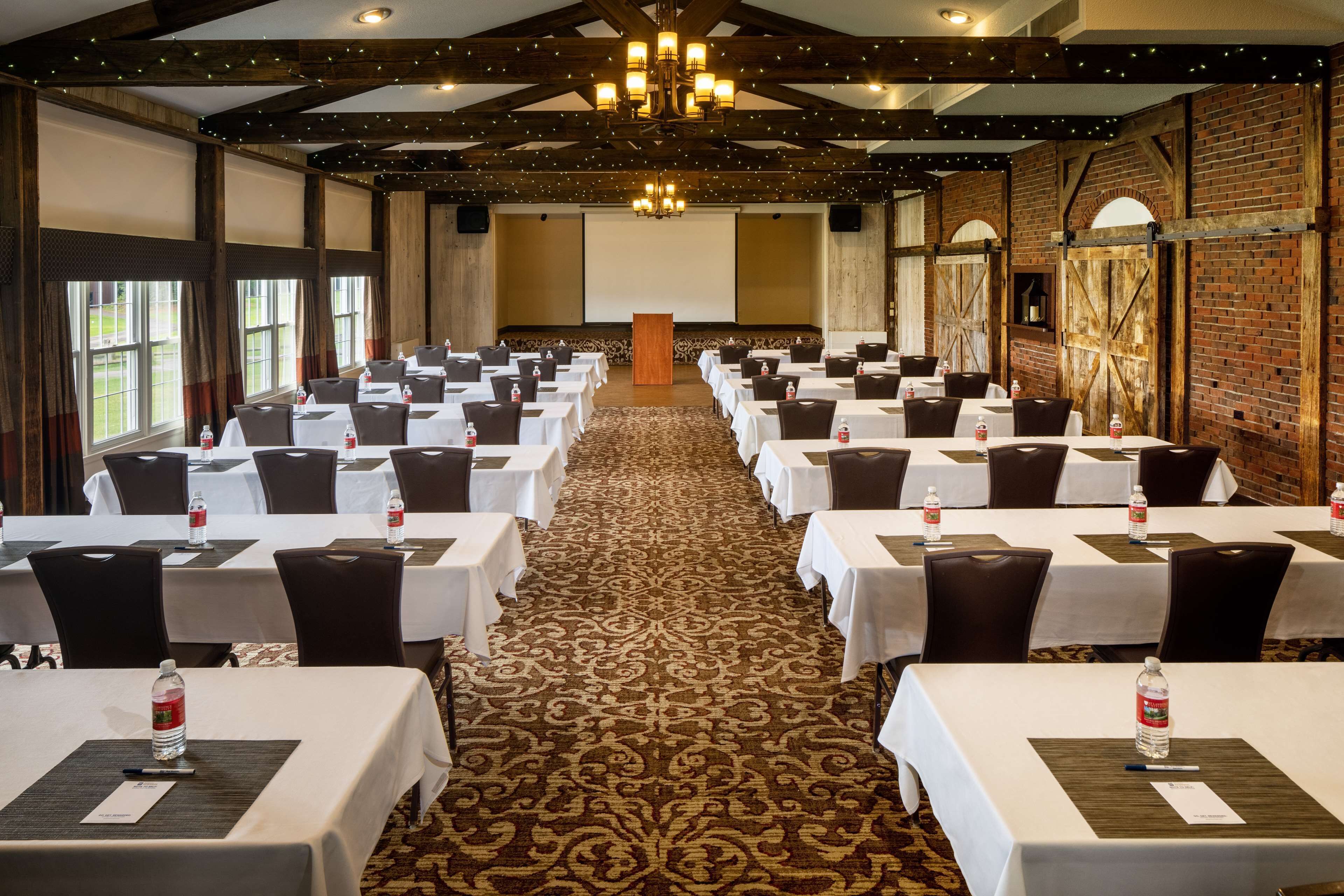 A conference room with rows of tables and chairs, a carpeted floor, and a wooden ceiling with exposed beams.