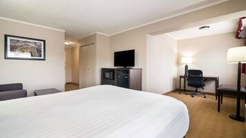 Una habitación de hotel con una cama grande, un escritorio con silla, un televisor, una lámpara y un cuadro en la pared.