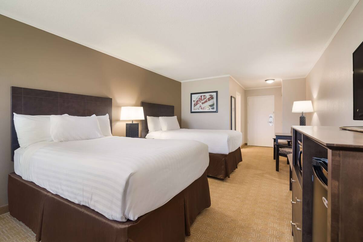 A hotel room with two beds, a desk, and a TV.