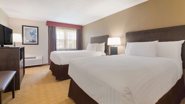 A hotel room with two beds, a desk, a television, and a framed picture on the wall.