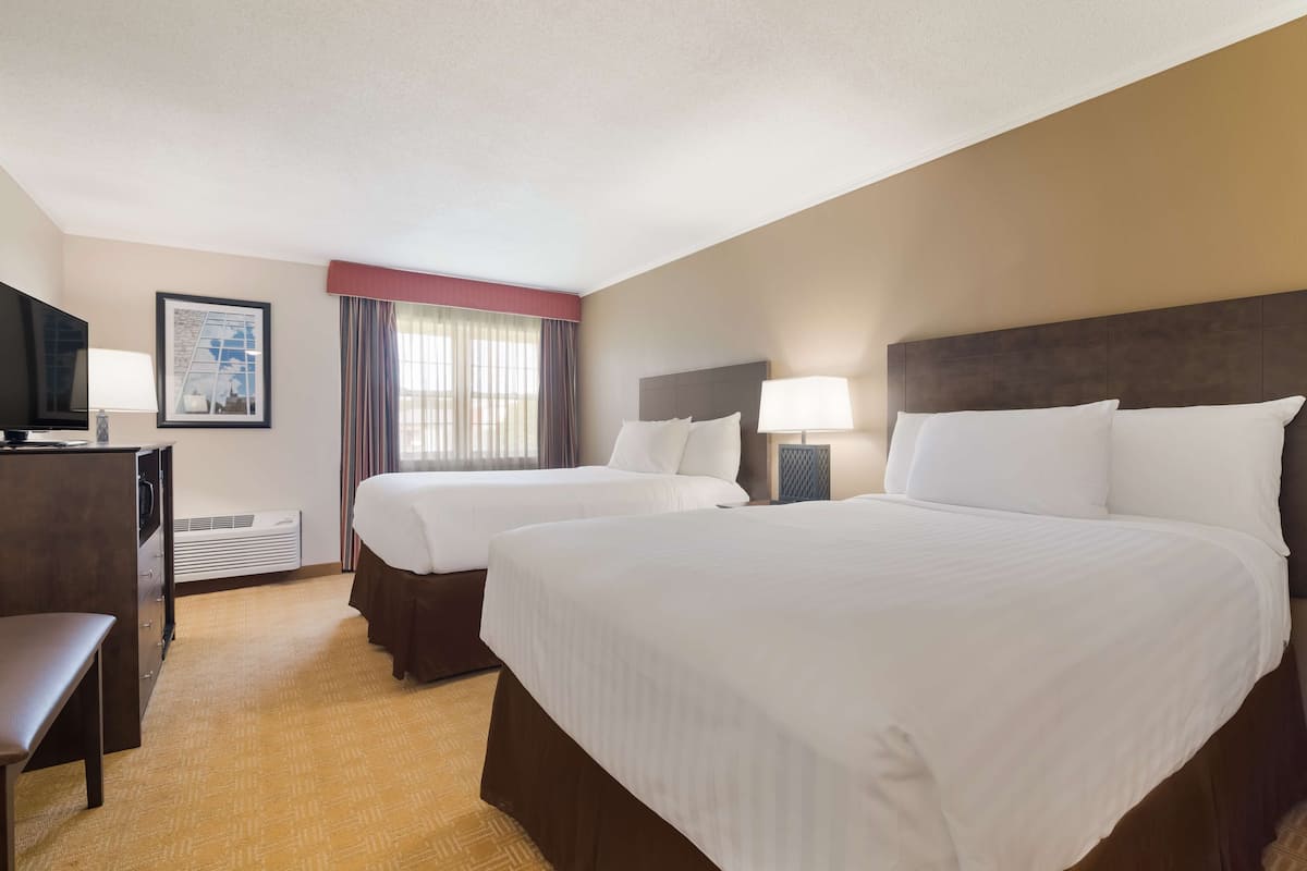 A hotel room with two beds, a desk, a television, and a framed picture on the wall.