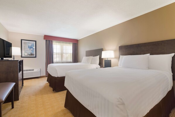 A hotel room with two beds, a desk, a television, and a framed picture on the wall.