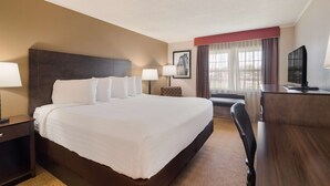 A hotel room with a large bed, bedside tables, a desk, a chair, and a television.