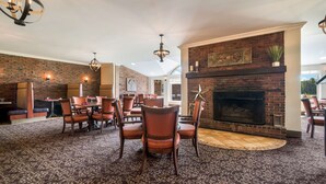 A spacious dining area with a brick fireplace, modern lighting fixtures, and a patterned carpet.