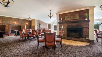 A spacious dining area with a brick fireplace, modern lighting fixtures, and a patterned carpet.