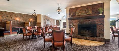 A spacious dining area with a brick fireplace, modern lighting fixtures, and a patterned carpet.