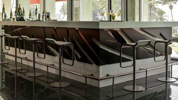 Un espace bar avec un comptoir, des tabourets et une vue sur les palmiers à travers de grandes fenêtres.