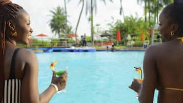 Dos personas junto a una piscina con palmeras al fondo.