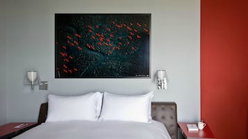Una habitación de hotel con una cama grande, una mesita de noche, una pared de acento roja y un cuadro de pájaros en la pared.