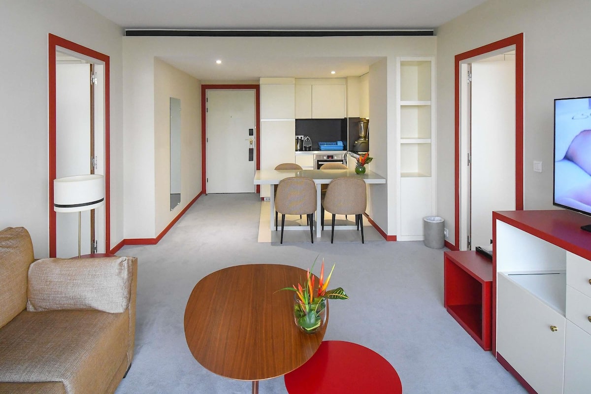 A modern hotel room with a dining area, kitchenette, and a TV.