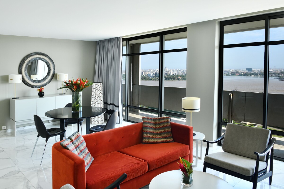 Une chambre d’hôtel moderne avec un canapé rouge, une table à manger et une vue sur une rivière.