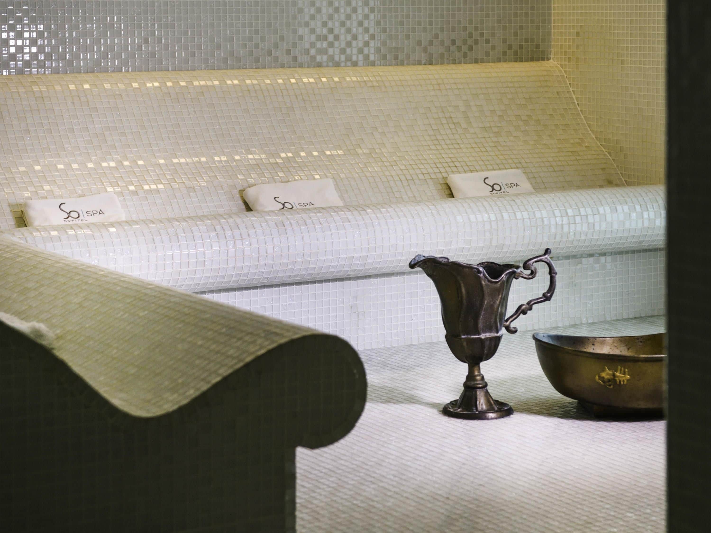 A room with a white sofa, a metallic pitcher, and a bowl on a table.