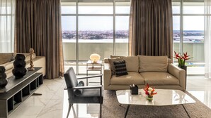 Un salon moderne avec un canapé, un fauteuil, une table basse et une vue sur le paysage urbain, visible à travers de grandes fenêtres.