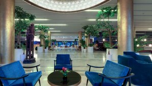 Un hall d’entrée spacieux, doté de sièges bleus, de grandes colonnes et de plantes en pot.