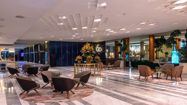 Un hall d’entrée spacieux, doté d’un sol en marbre, de meubles modernes et d’un espace de réception avec un écran numérique.