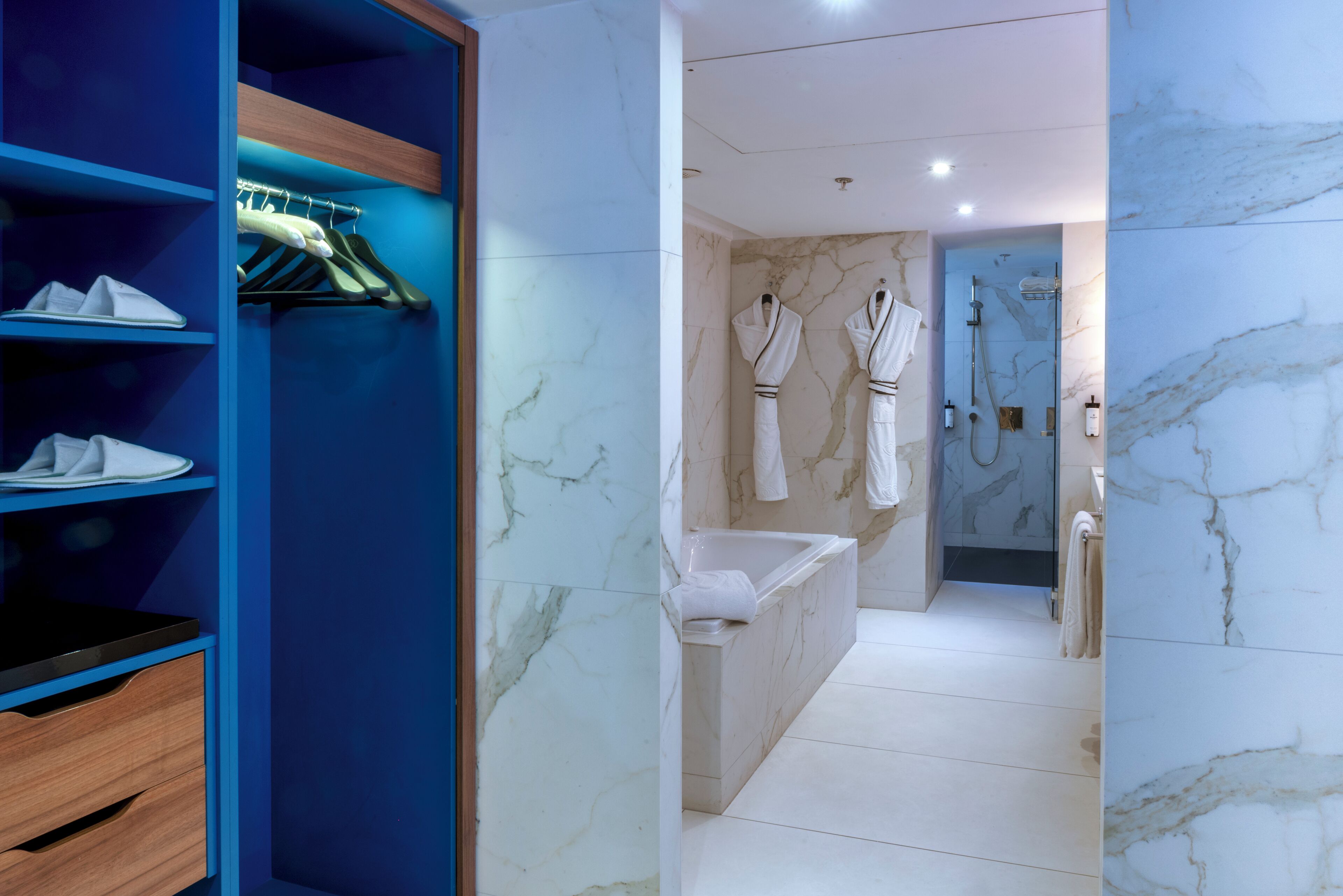 Une salle de bain moderne avec un sol en marbre, une baignoire et deux peignoirs blancs accrochés au mur.