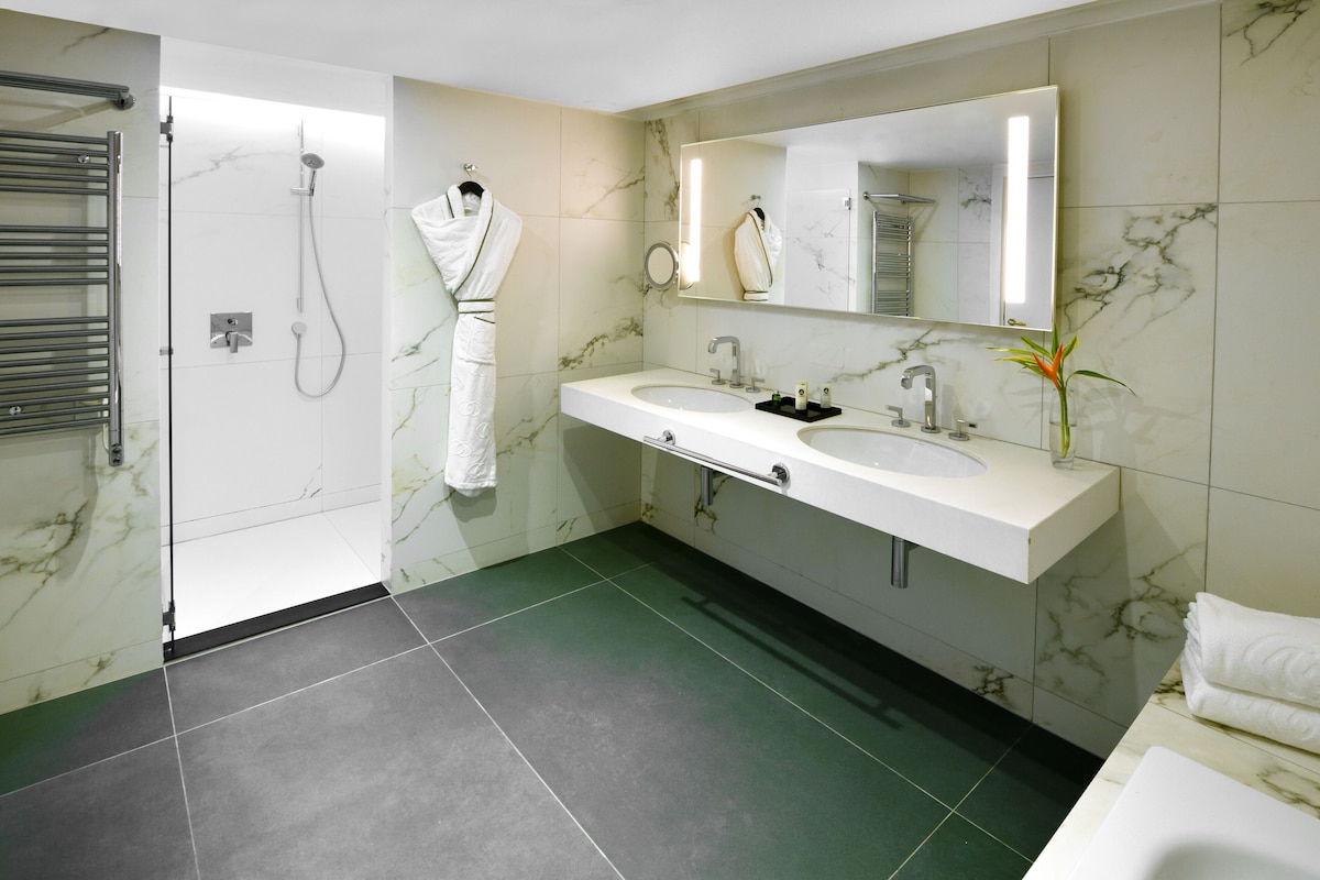 Une salle de bain moderne avec une douche à parois de verre, deux vasques, un grand miroir et un porte-serviettes.