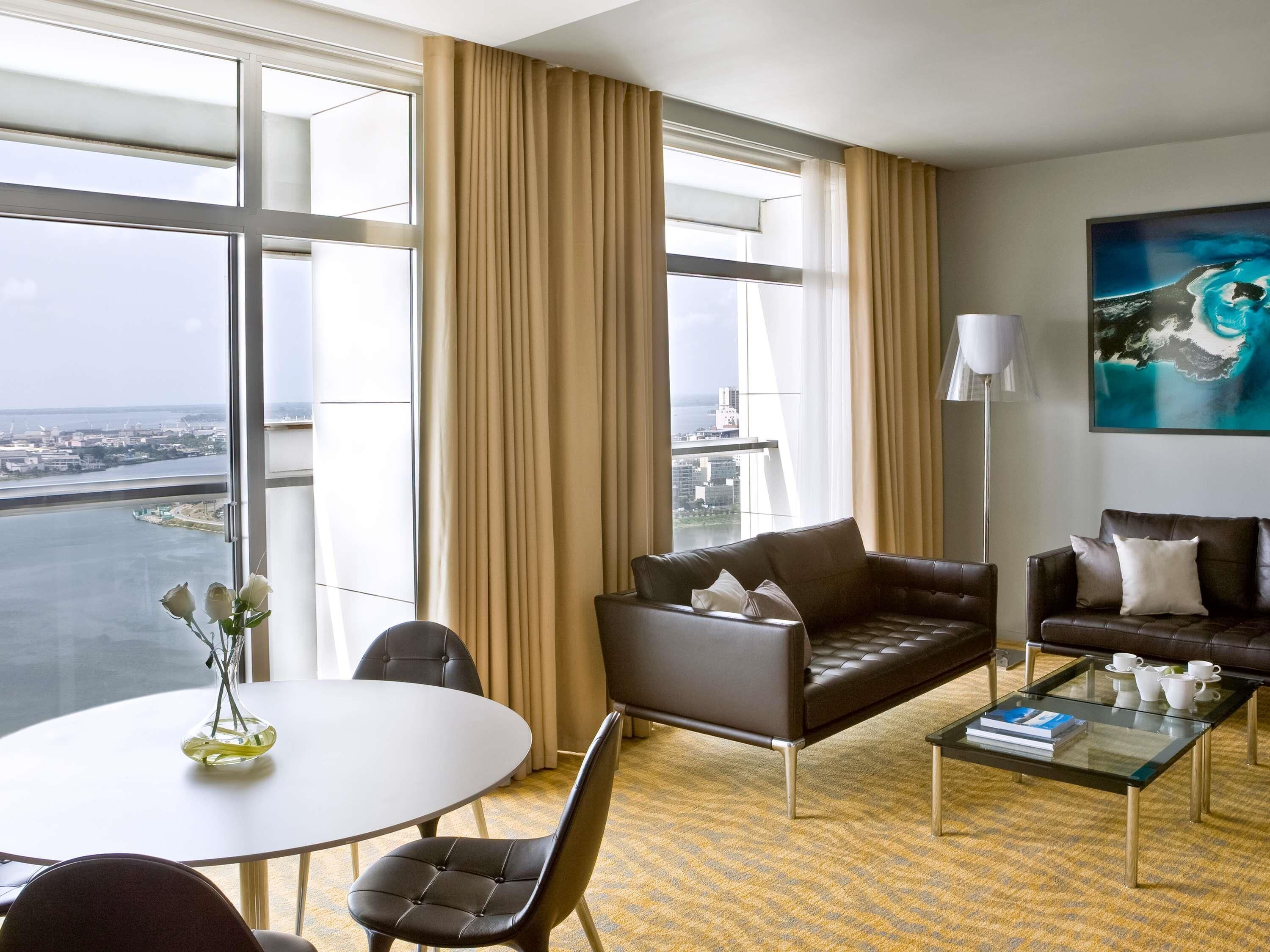 A hotel room with a large window, a sofa, a coffee table, and a painting.