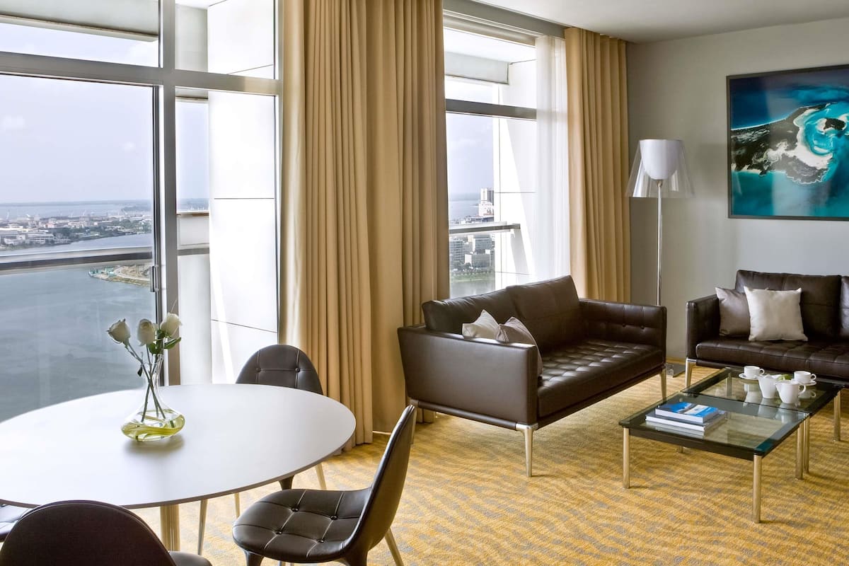 A hotel room with a large window, a sofa, a coffee table, and a painting.