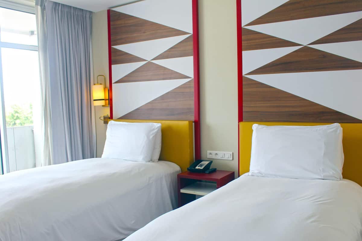 Una habitación de hotel con dos camas, una mesita de noche con un teléfono y una ventana con cortinas.