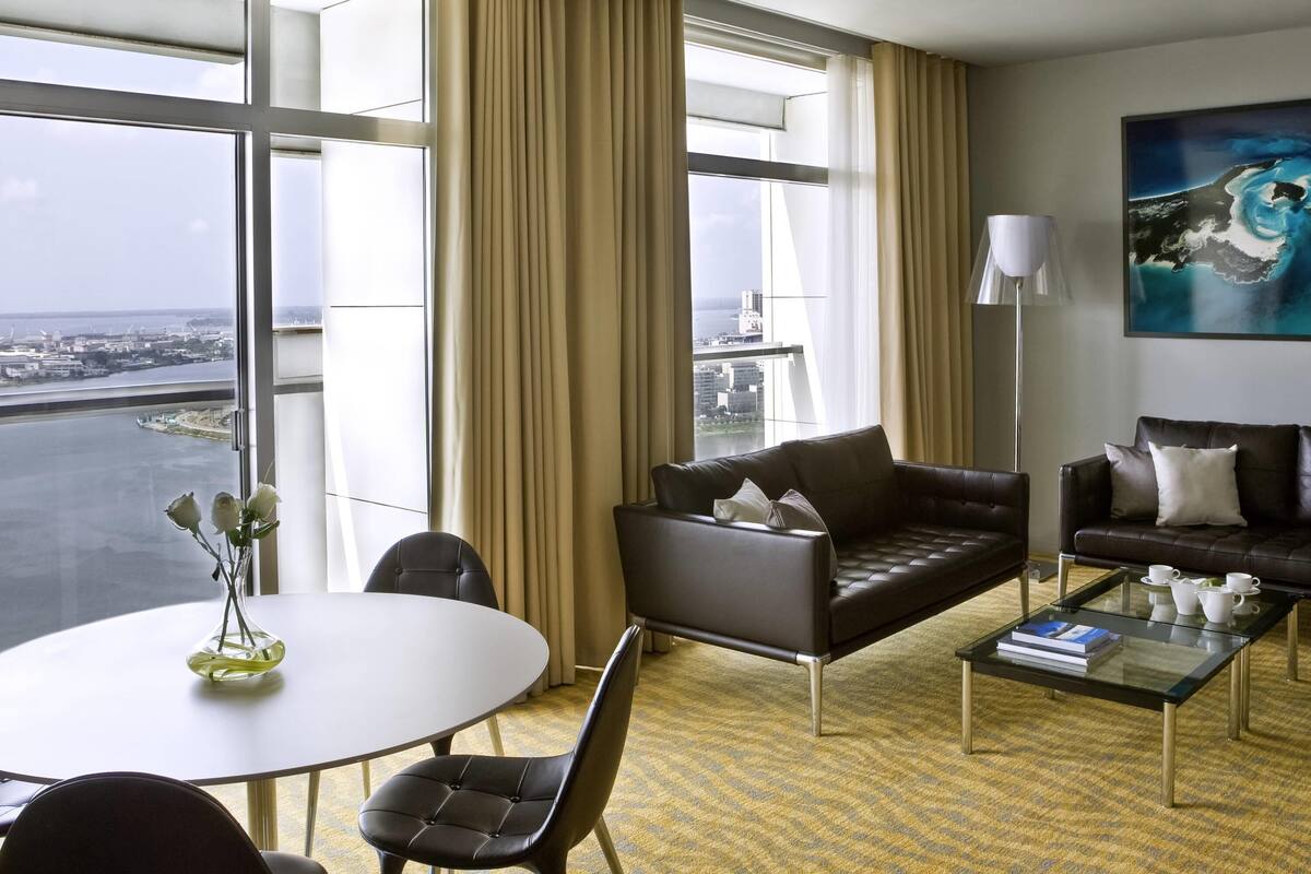 A modern hotel room with a large window, a sofa, a coffee table, and a painting on the wall.