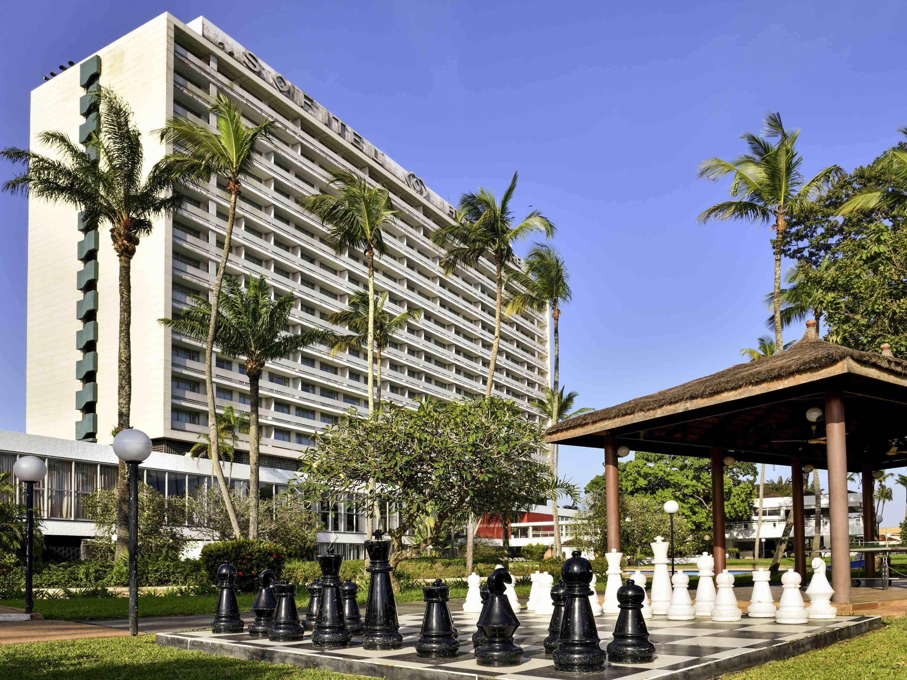 A hotel with a large building, palm trees, and a chessboard with chess pieces.