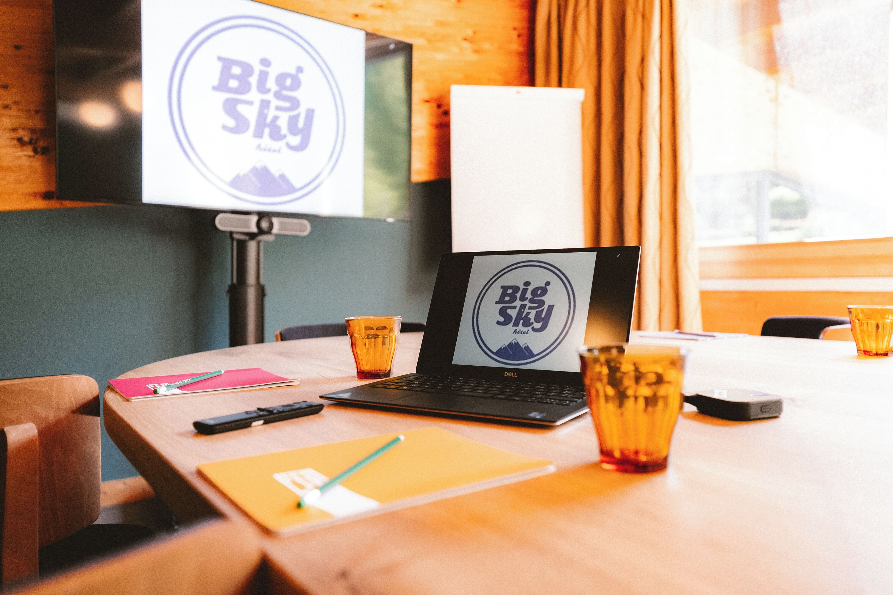 A hotel room with a wooden table, a laptop, a television, and two glasses of a beverage.