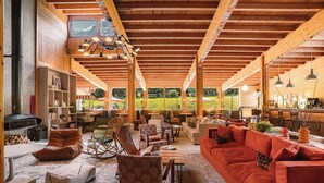 A spacious living area with wooden beams, a fireplace, and a large window offering a view of the outdoors. -  Big Sky Hotel & Spa (Chamonix-Mont-Blanc)