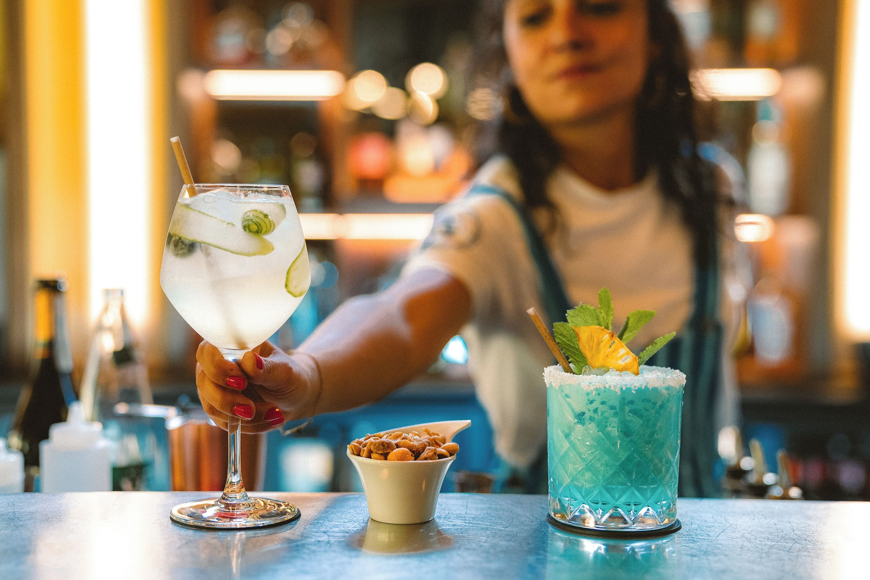Een barsetting met twee drankjes, een in een glas en een in een longdrinkglas, en een kleine schaal met noten op de toonbank.