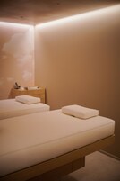 A modern bedroom with two beds, a wooden nightstand, and a wall-mounted shelf.