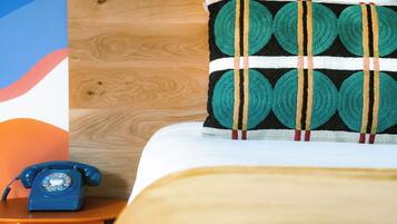 Ein Bett mit einem gemusterten Kopfkissen, einem Holz-Kopfteil und einem blauen, alten Telefon auf einem Nachttisch aus Holz.