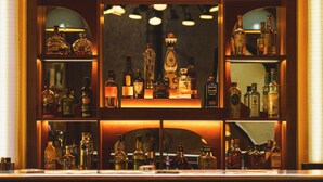 A bar area with shelves of various liquor bottles and a neon sign that reads "DRINKS". -  Big Sky Hotel & Spa (Chamonix-Mont-Blanc)